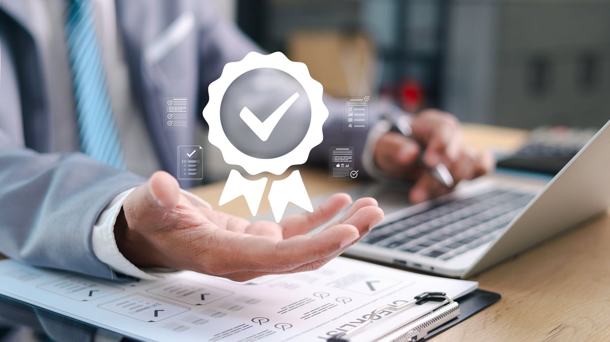 Businessman presenting quality certification badge with check mark over documents and laptop. Concept of approval, compliance, audit, trust, and business standards.